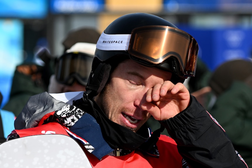 Still wearing his helmet, Shaun White wipes a tear away from his eye