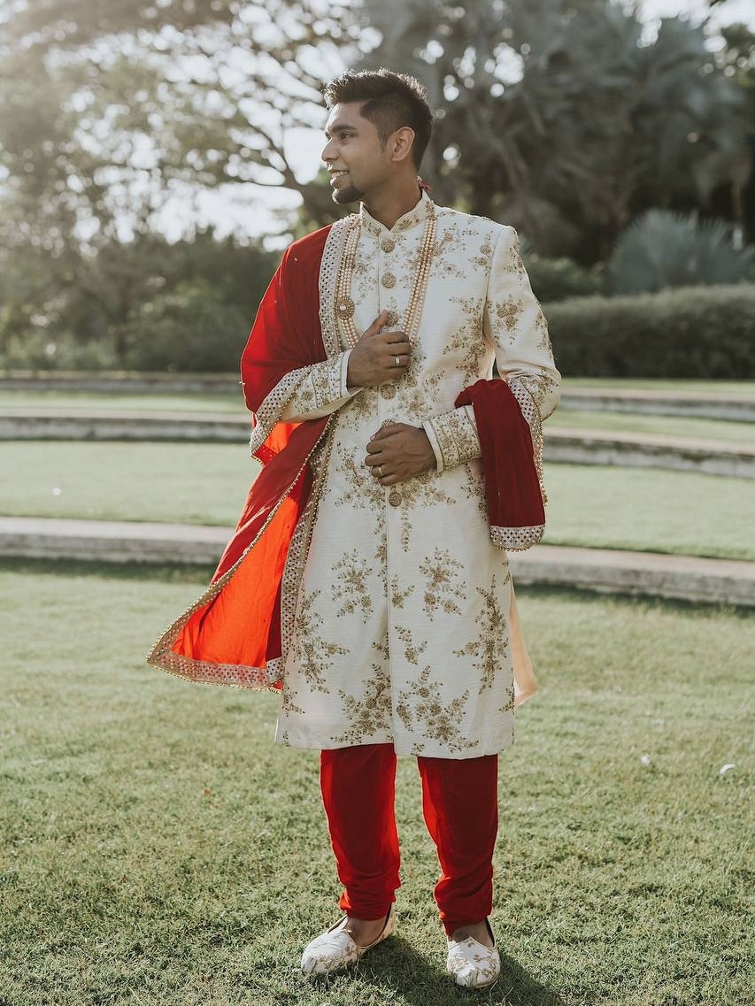 A man dressed in a Indian formal suit called the Sherwani standing on a lawn.