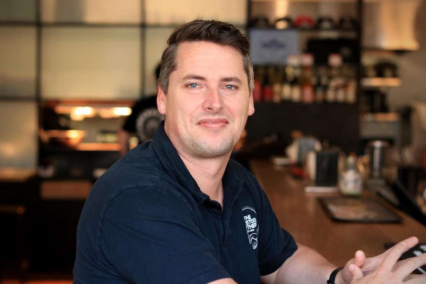 Lachlan Stevens sits at the bar wearing a black t-shirt.