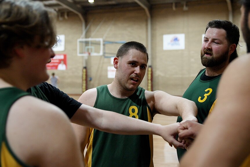 Group of men wearing green basketball singlets in a huddle. 