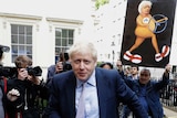 Boris Johnson walks in front of a media scrum in front of a white Georgian building in London.