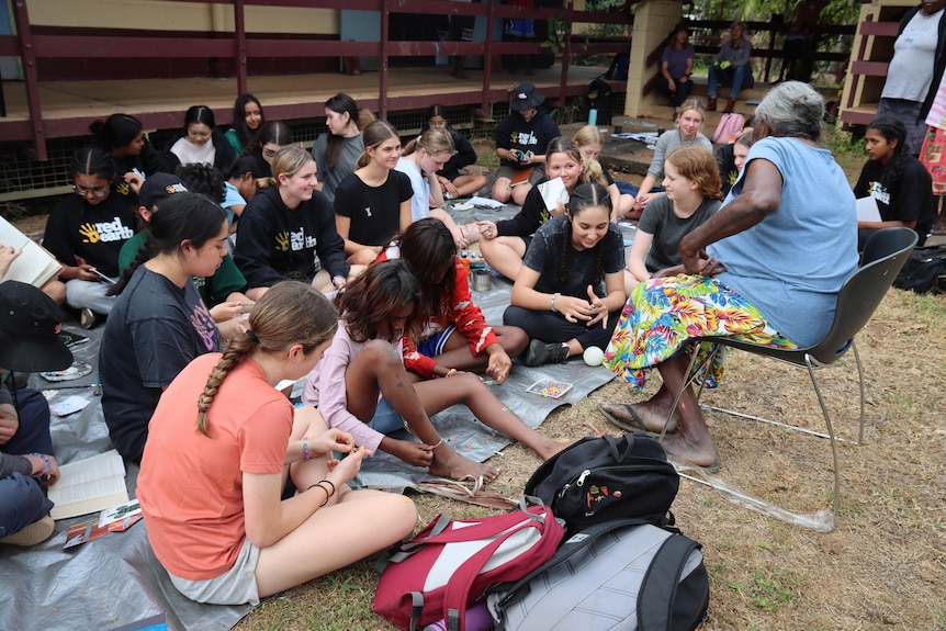 A woman outside teaching a class of students sitting down.