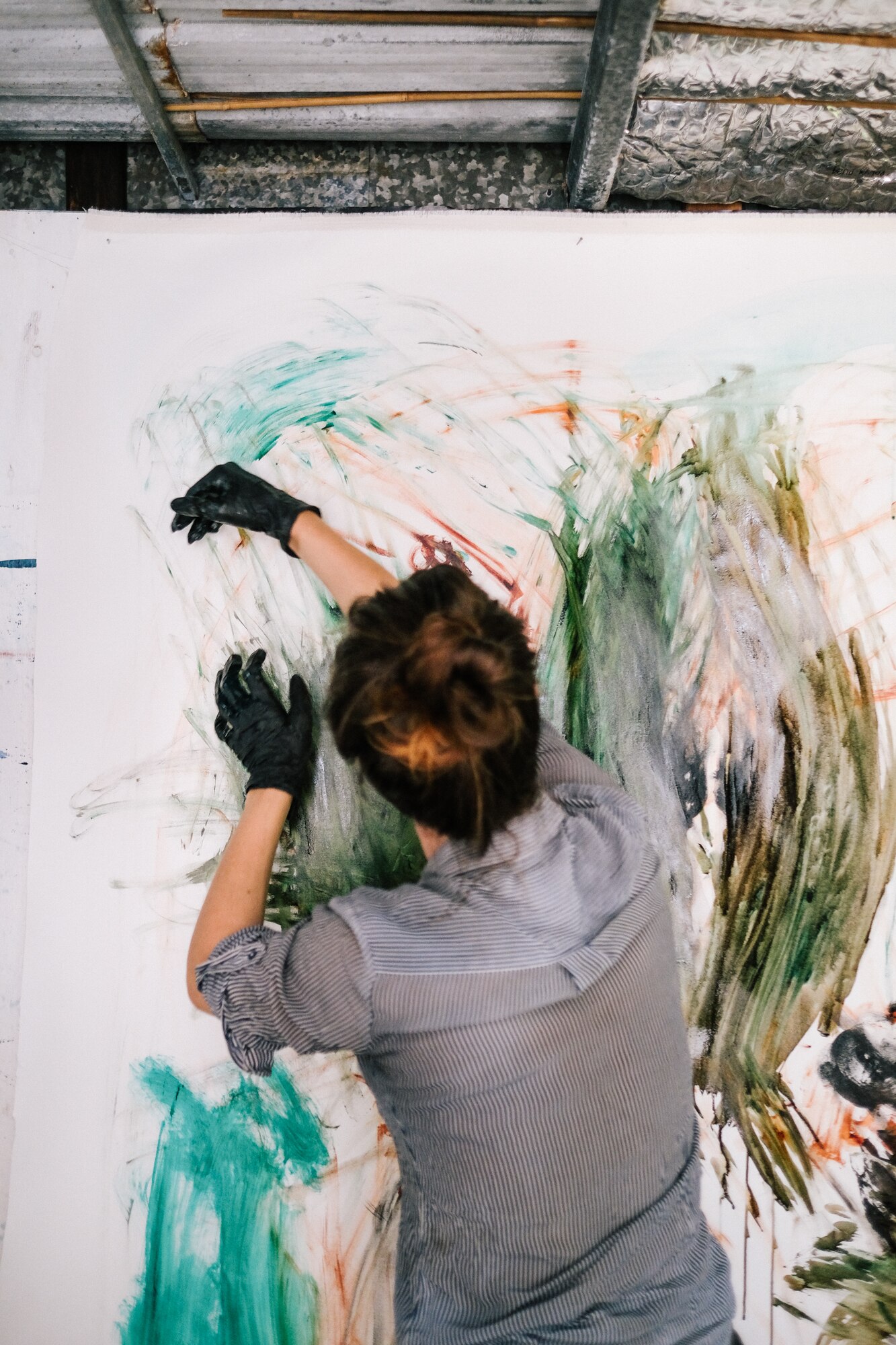 Walker at work in her studio. With forceful movement, she drags her black gloves covered with paint across the canvas.