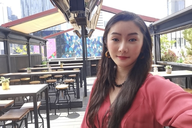 A woman sits in a rooftop bar with te Melbourne skyline behind her.