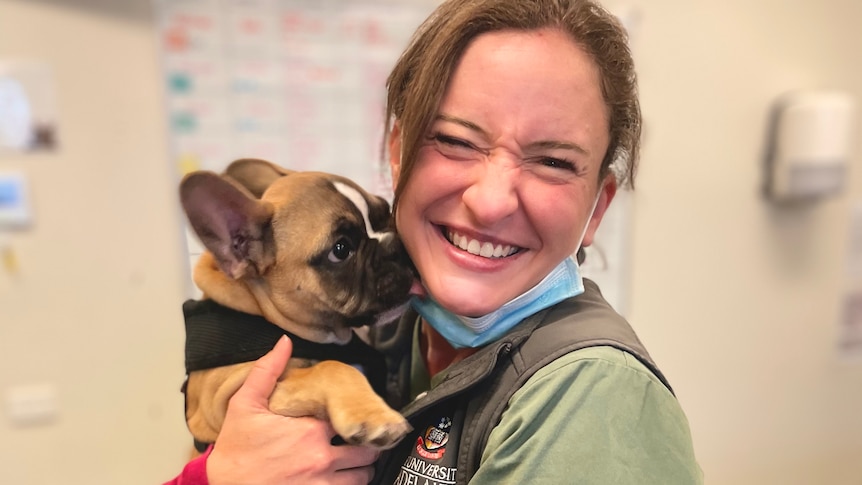 A young woman cuddles a French Bulldog with a big smile on her face