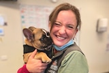 A young woman cuddles a French Bulldog with a big smile on her face