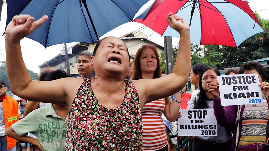 A woman raises her arms as she cries during the funeral march of Kian delos Santos.