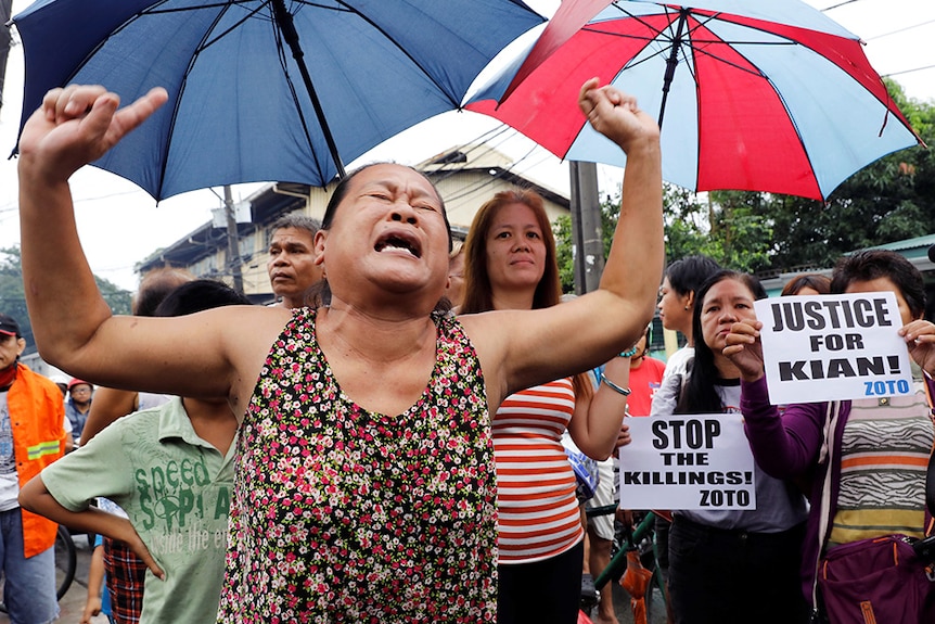 A woman raises her arms as she cries during the funeral march of Kian delos Santos.