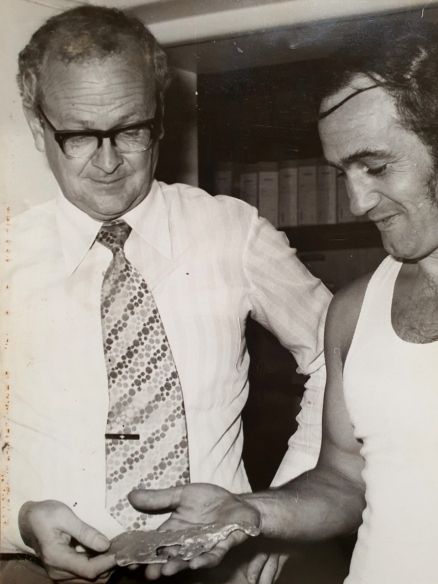 A black-and-white image of a man handing a bank manager a golden nugget.