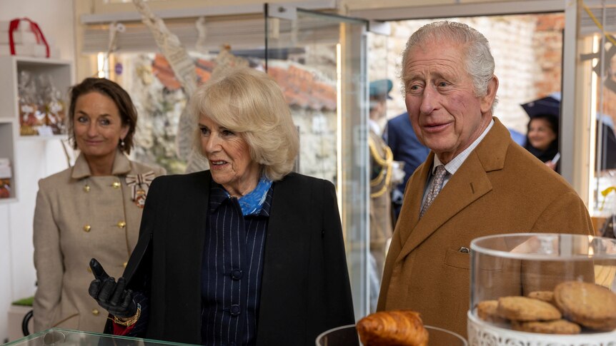 Charles and Camilla stand together at the counter of a bakery.