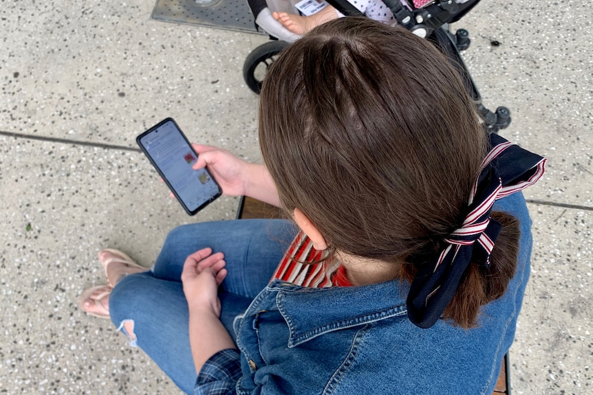 A woman is sitting on a chair scrolling through her phone
