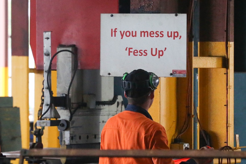 A man in hi vis stands in front of a sign that reads 'if you mess up, 'fess up'