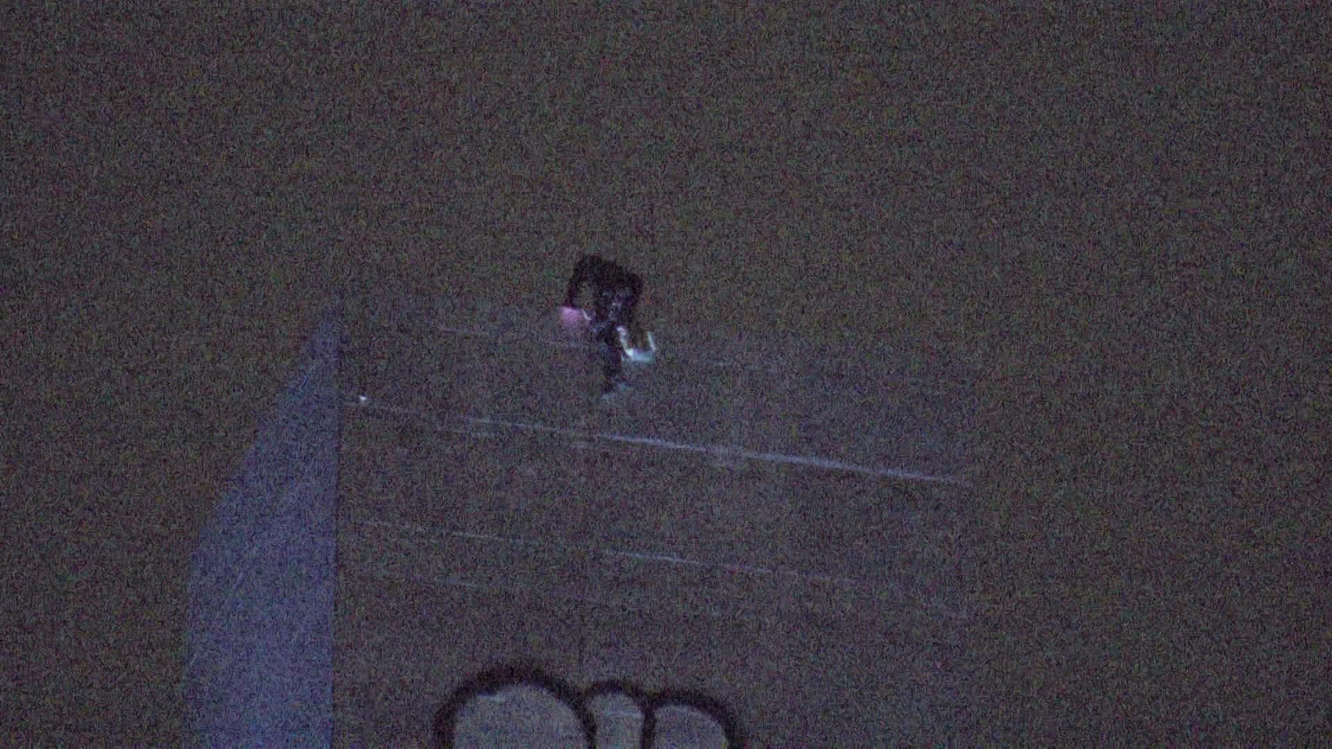A person dressed entirely in black climbs over the edge of a concrete tower.