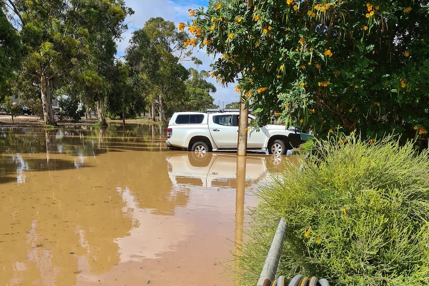 A photo of a parked car surrounded by a few centimetres of muddy water.
