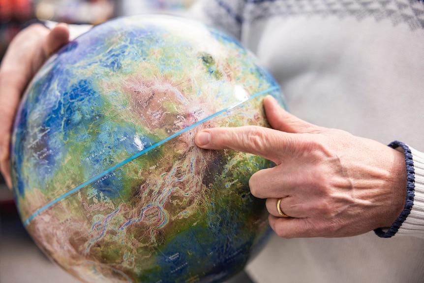 Finger pointing to location on globe of Venus