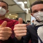 Two men wearing face masks and doing thumbs up.