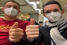 Two men wearing face masks and doing thumbs up.