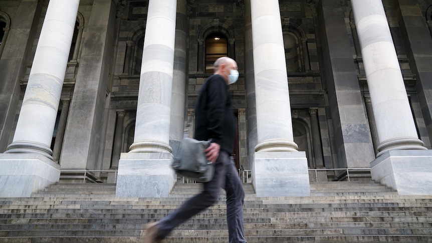 A man with a face mask walks past large columns and steps