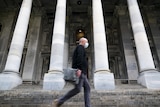 A man with a face mask walks past large columns and steps