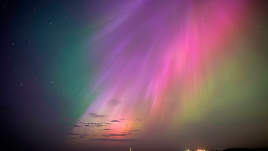 A view of a sky with rainbow and pink light streaks coming down.