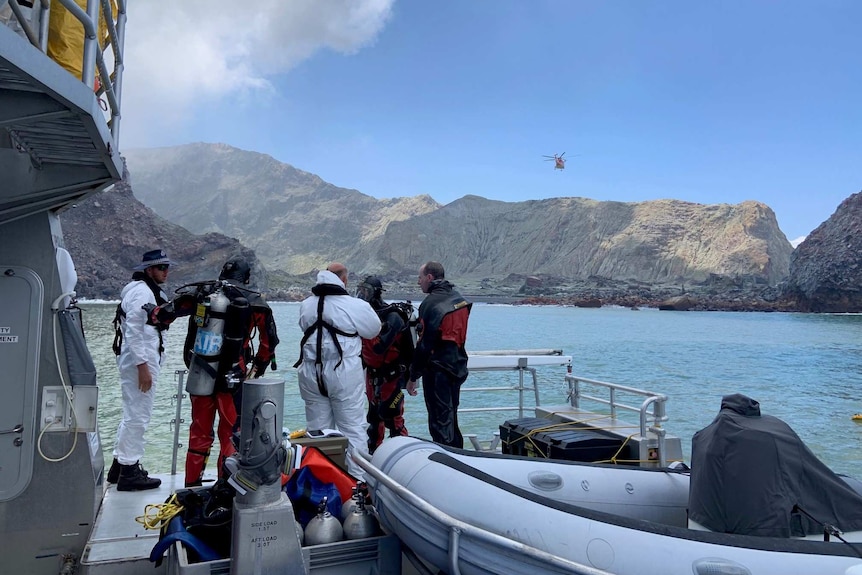 Some divers standing on a boat with an island in the background