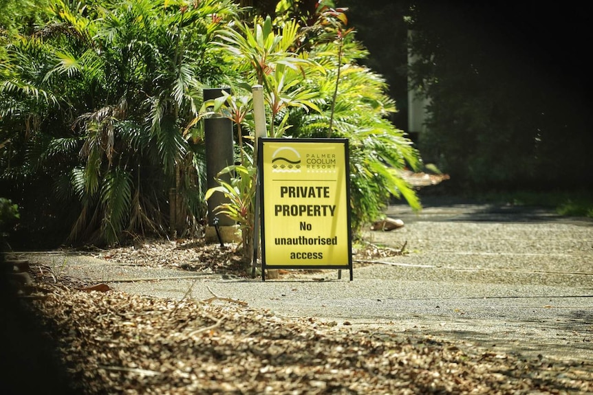 A yellow 'private property' sign on a path near palm trees.