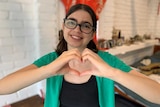 Young woman wearing glasses, makes love heart sign with her hands