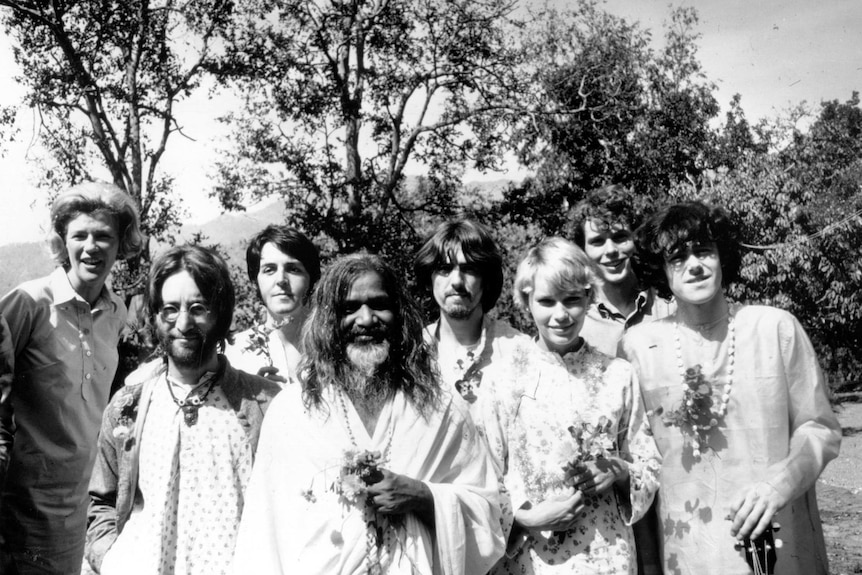 Black and white photo of yogi Maharishi Mahesh with long hair alongside members of The Beatles.
