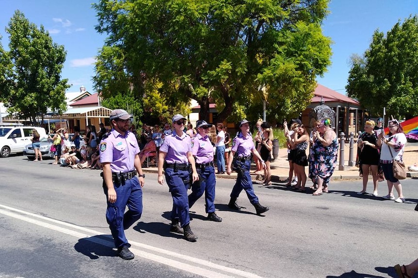 A line of four police in uniform march in a street parade.