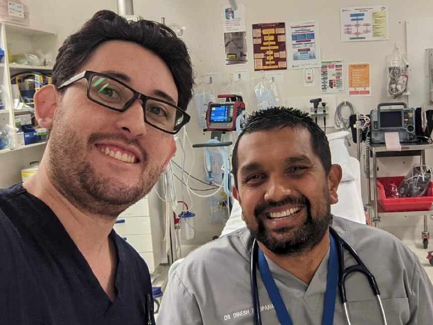 Two smiling male doctors take a selfie in a hospital.