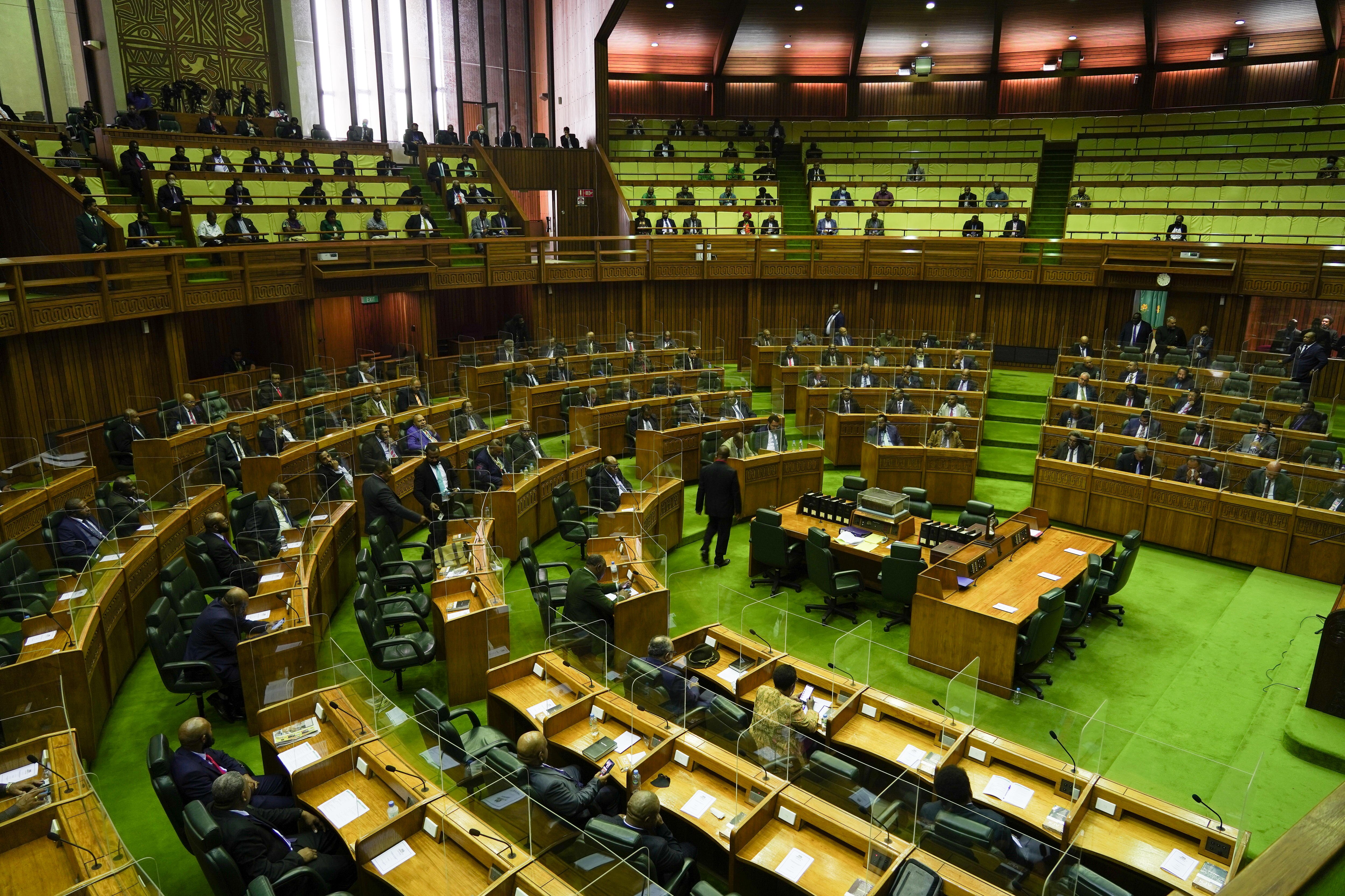 Politicians sit at their seats in a bright green carpeted chamber.  Several chairs are empty