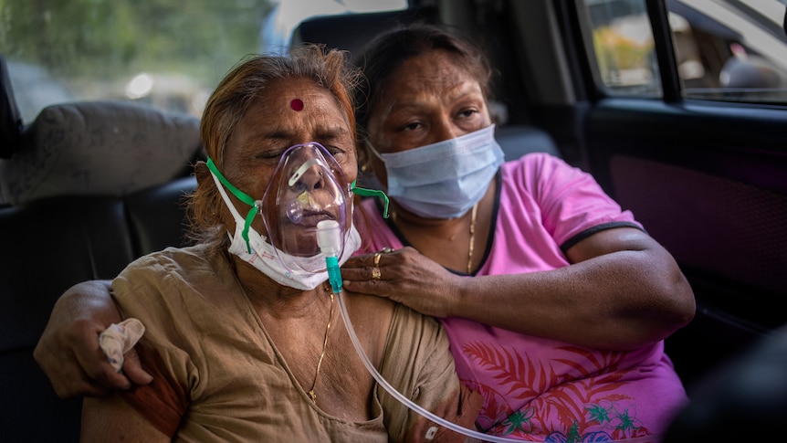 A COVID-19 patient receives oxygen in the back of a car