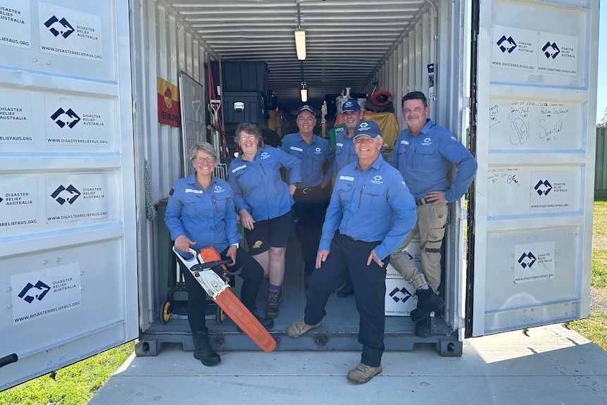 Six members of Disaster Relief Australia smile in the back of a shipping container.