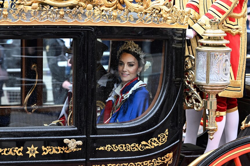A woman in a tiara and blue cape in a carriage 