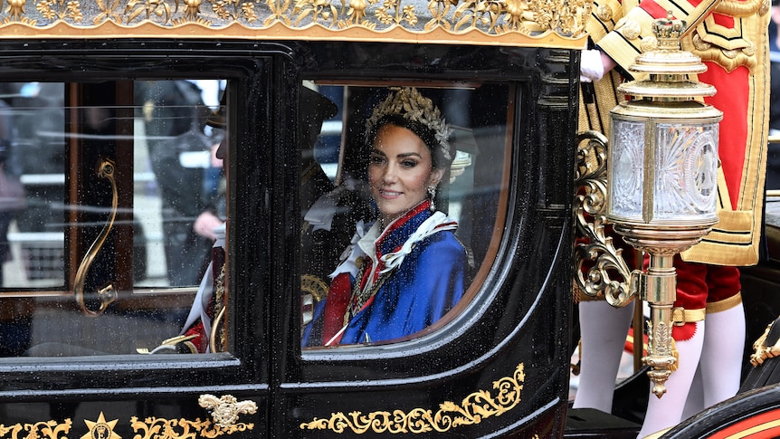 A woman in a tiara and blue cape in a carriage 