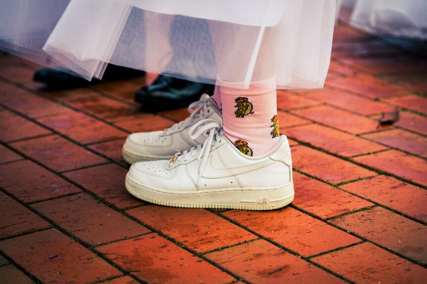 A close-up of white sneakers and pink socks under a formal dress.
