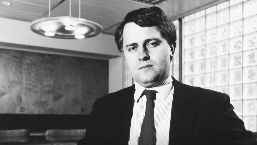 A young Malcolm Turnbull sits in an office wearing a suit. The picture is clearly dated, in black and white.