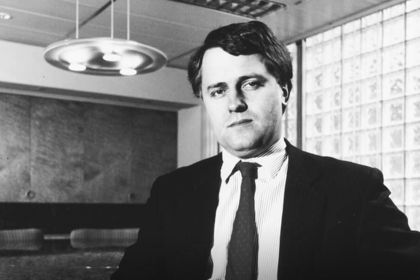 A young Malcolm Turnbull sits in an office wearing a suit. The picture is clearly dated, in black and white.