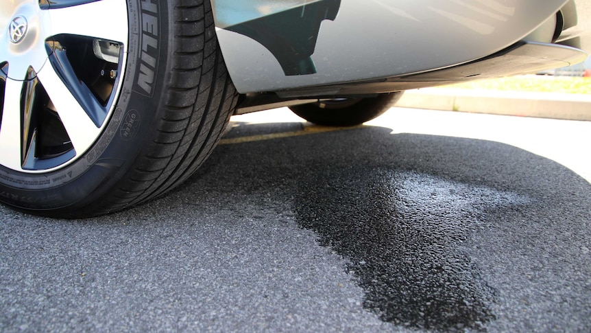 Close up of the rear wheel and back section on a hydrogen car, with a patch of water on the ground.