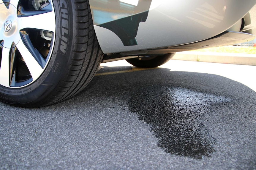 Close up of the rear wheel and back section on a hydrogen car, with a patch of water on the ground.