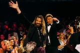 Scott Maxwell waving as he walks through a crowd holding his ARIA award.