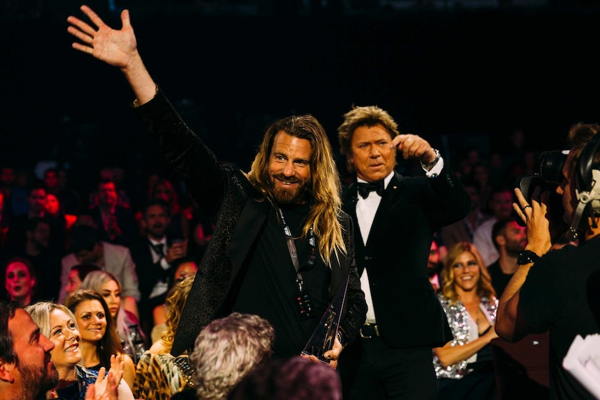 Scott Maxwell waving as he walks through a crowd holding his ARIA award.