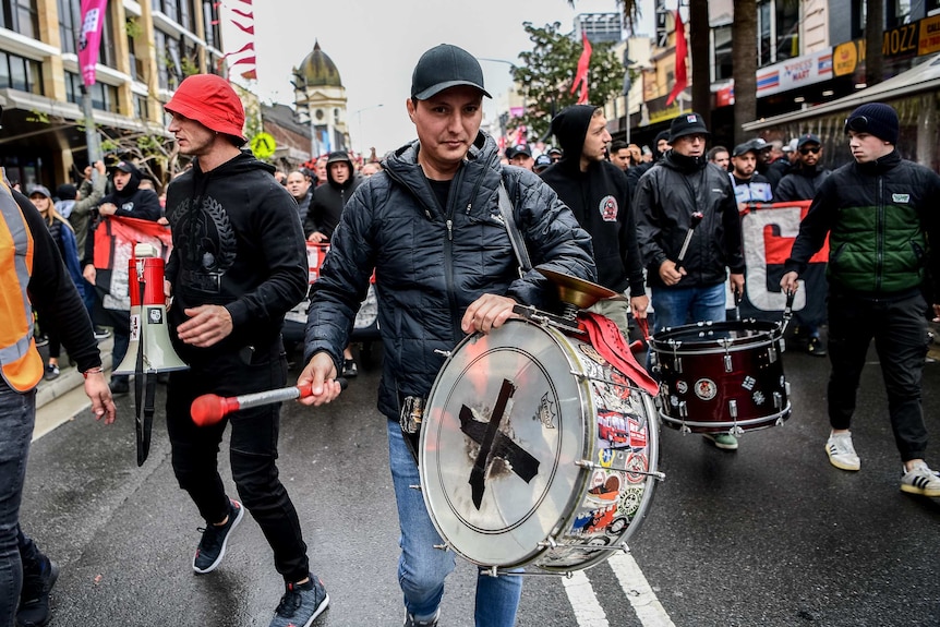A man with a bass drum strapped to him leads an RBB parade.
