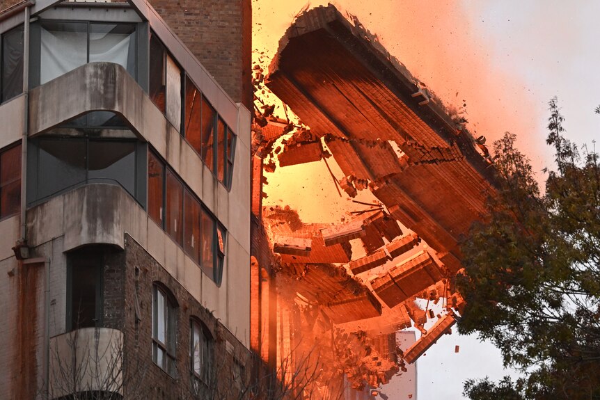 A wall falls off a burning building 