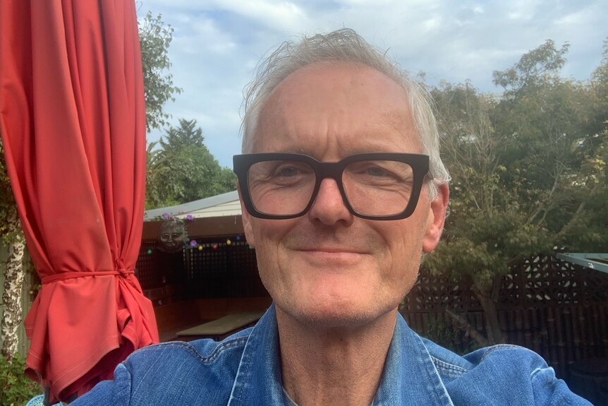 An older man wearing glasses and smiling takes a selfie.