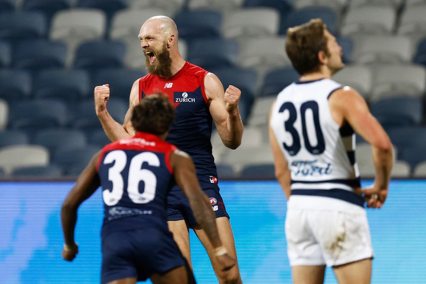 A bald, bearded Melbourne AFL player punches the air with his fists and roars in delight as a teammate runs toward him.   
