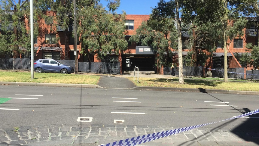 A police car sits on the road in front of police tape.