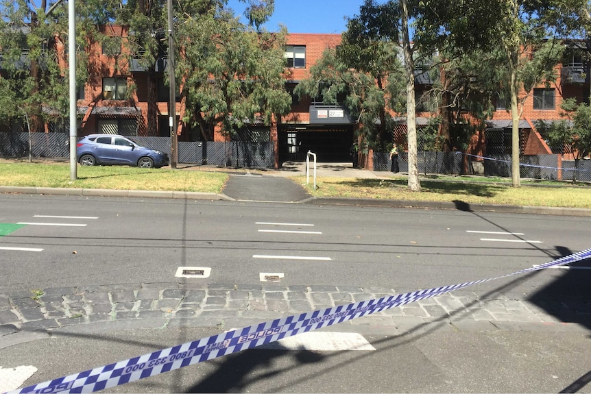 A police car sits on the road in front of police tape.