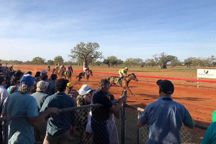 A crowd watches on as horses approach the finish line at a country race club.