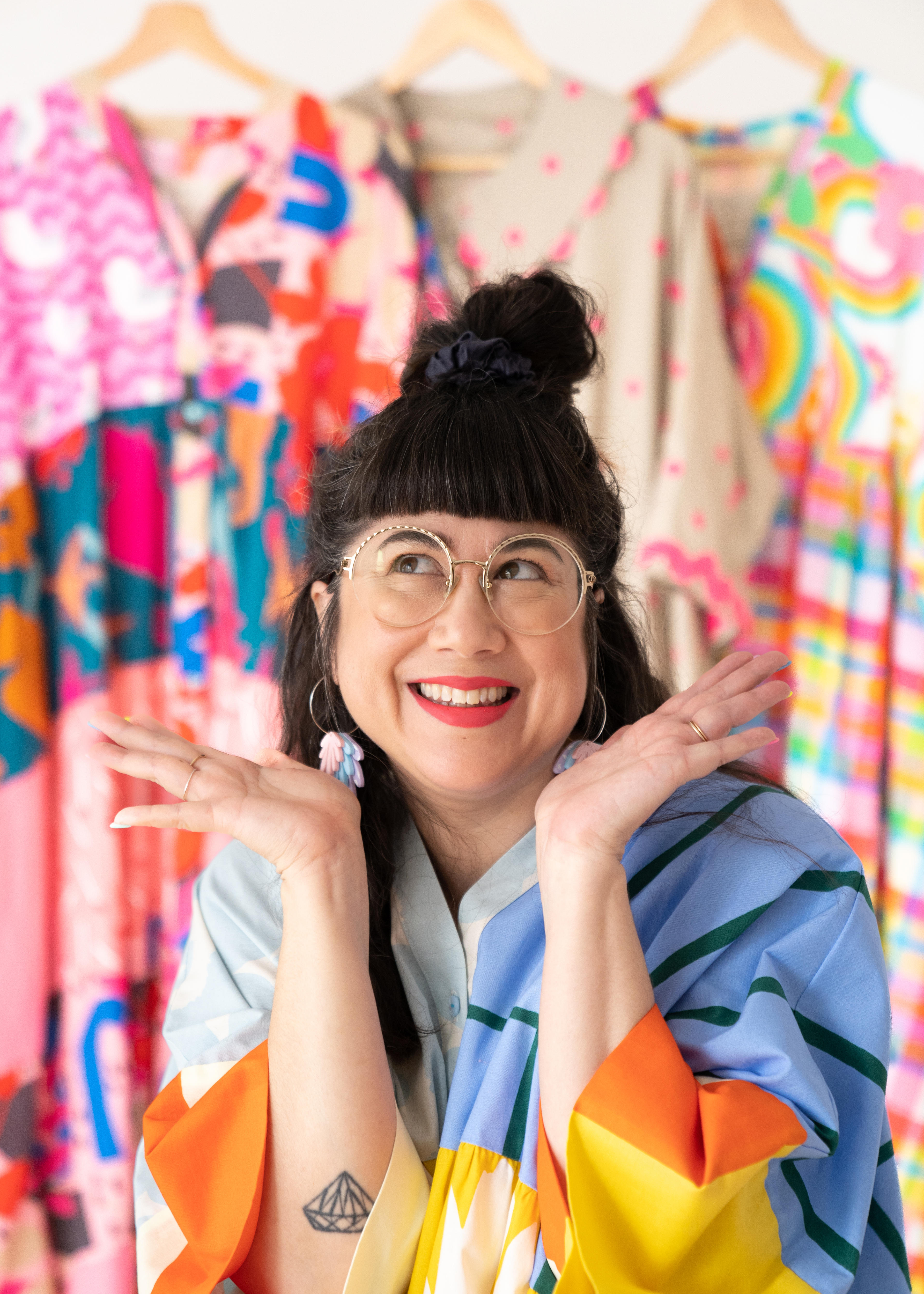 Sue-Ching Lascelles smiling with her hands up and wearing colourful clothing